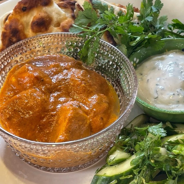 Chicken Tikka Masala on a plate with raita, flatbread and cucumbers