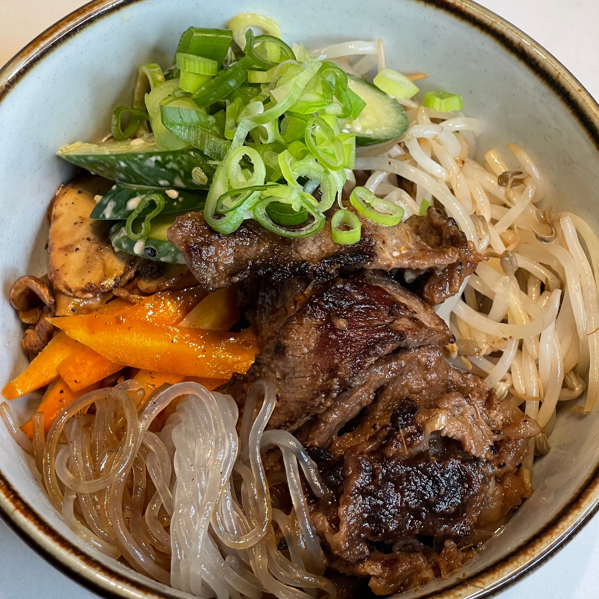 A bowl of Korean Bulgogi Beef & Glass Noodles with sliced beef, glass noodles, and vegetables garnished with green onions.